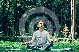 Young attractive man in sport clothes is meditating in the lotus position with a pacified face in the park photo