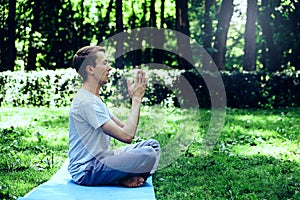 Young attractive man in sport clothes is meditating in the lotus position with a pacified face in the park photo