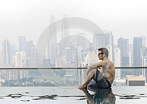 Young attractive man at the swimming pool in roof at skyscraper.