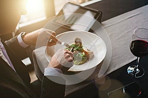 A young and attractive man uses his tablet while eating turkey fillet roll and pea puree in an indoor restaurant