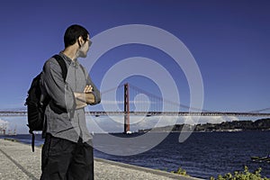 A young attractive man walking along the riverside of Tejo river in the city of Lisbon in Portugal. The April 25th bridge in the photo