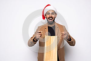 Young attractive man wearing Santa hat holding and pointing red shopping bag in christmas consumerism , December sale, buying xmas