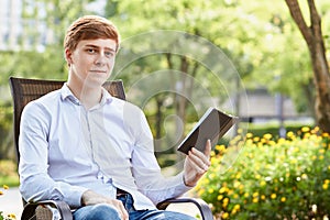 Young attractive man in white shirt sitting on brown chair in the park on green background
