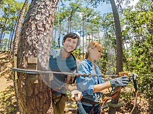 Young attractive man and woman in adventure rope park in safety equipment