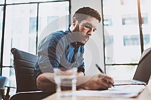 Young attractive man working at sunny loft office on laptop while sitting at wooden table.Businessman analyze digital