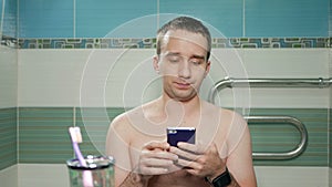 Young attractive man writing sms on the phone in the bathroom of the hotel room. Without T-shirts with a naked torso