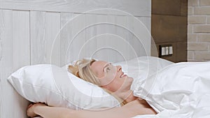 Young attractive middle-aged blonde woman in a white coat wakes up in the morning in bed.