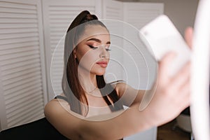 Young attractive model make a selfie after makeup in beauty studio. She use a ring lapm for photo. Background of white