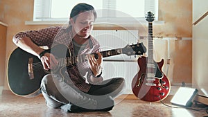 Young attractive musician plays the guitar sitting on the floor in the kitchen