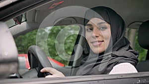 Young attractive muslim girl in hijab is sitting in car, watching at camera, religiuos concept, transport concept