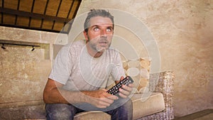 Young attractive nervous and excited man sitting at home living room couch holding TV remote watching football game or suspense