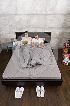 Young attractive pair reading books while lying in the bed in th