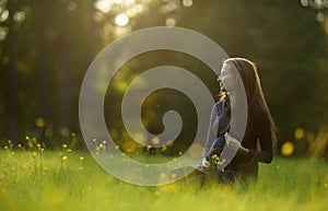 Young attractive pregnant woman in dress sitting on green meadow at sunset. 9 months pregnancy. Expecting child