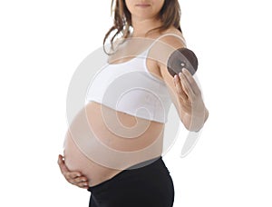 Young attractive pregnant woman holding her big belly with hand and eating chocolate donut