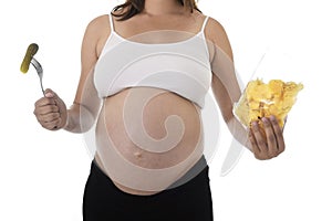 Young attractive pregnant woman showing big belly eating chips holding pickle with fork photo