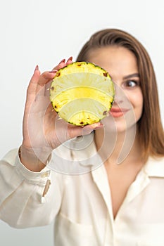 A young attractive pretty nice caucasian smiling woman holds ring slice pineapple covering her eye against a white
