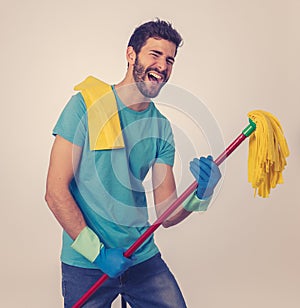 Young attractive proud man holding mop as microphone having fun while cleaning