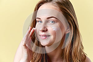 Young attractive redhead woman applying moisturiser face cream, smiling and looking at camera. Beauty, skincare.