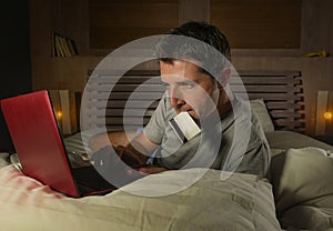 Young attractive and relaxed man at home bedroom lying on bed buying or banking online using credit card for paying in electronic
