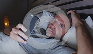 Young attractive and relaxed man at home bedroom networking late night lying on bed in dark light using mobile phone enjoying