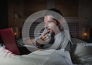 Young attractive and relaxed man networking at home lying comfortable on bed late night happy watching movie on laptop computer or