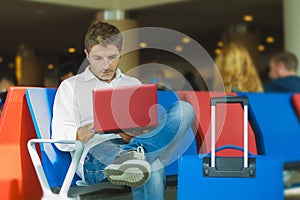 Young attractive and relaxed traveler man with luggage working with laptop computer waiting for flight at airport departure lounge