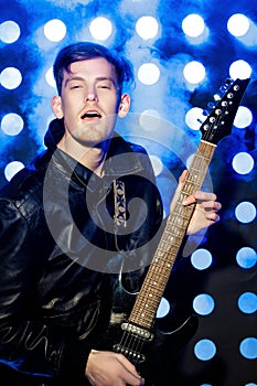 Young attractive rock musician playing electric guitar and singing. Rock star on background of spotlights