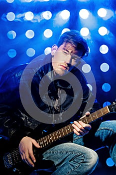 Young attractive rock musician playing electric guitar and singing. Rock star on background of spotlights