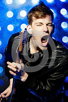 Young attractive rock musician playing electric guitar and singing. Rock star on background of spotlights