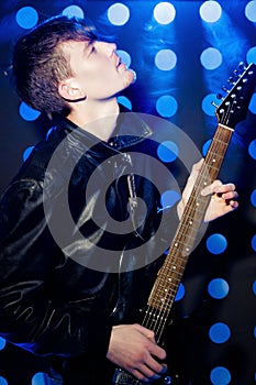 Young attractive rock musician playing electric guitar and singing. Rock star on background of spotlights