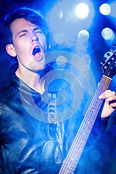 Young attractive rock musician playing electric guitar and singing. Rock star on background of spotlights