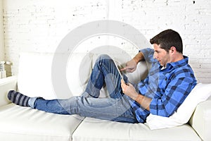 Young attractive 30s man using digital tablet pad lying on couch at home networking looking relaxed