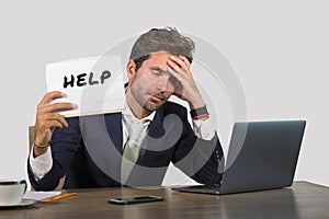 Young attractive sad and depressed business man working at office laptop computer desk holding notepad asking for help feeling des