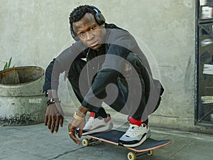 Young attractive and serious black African American man squatting on skate board at grunge street corner looking cool posing in