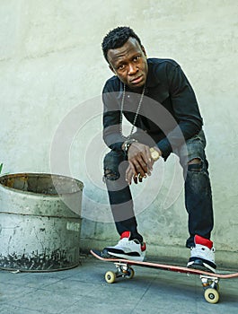 Young attractive and serious black African American man squatting on skate board at grunge street corner looking cool posing in