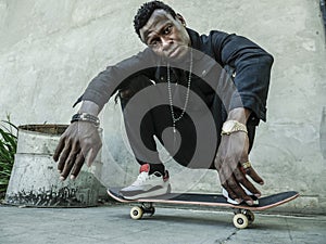 Young attractive and serious black African American man squatting on skate board at grunge street corner looking cool posing in