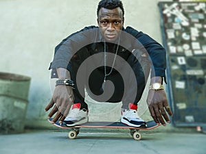 Young attractive and serious black afro American man squatting on skate board at grunge street corner looking cool posing in