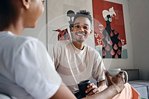 Young attractive smiling casual African American man joyfully looking in camera during coffee break in co-working space