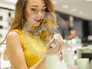 Young Attractive Smiling Girl in Yellow Dress is Tasting Scent of New Perfume in the Shopping Mall