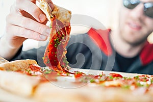 Young attractive smiling man eating pizza at street cafe. Cheat meal. Cheat day.