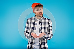 Young attractive smiling man in printed shirt and orange hat looks happy standing on blue background