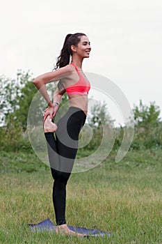 Young attractive smiling toned brunette woman stretching outside in a park. Healthy lifestyle concept