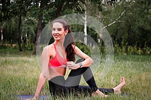 Young attractive smiling toned brunette woman stretching outside in a park. Healthy lifestyle concept