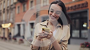 Young Attractive Smiling Woman Using her Smartphone Standing at the Old City Street. Communication concept.