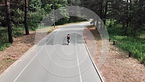 Young attractive sportive caucasian woman in pink jersey and black helmet is riding her bike in the summer forest. Aerial Drone sh