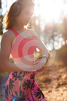 Young attractive sportswoman listening to music wearing headphones and checking her smart watch. Sport, fitness, workout