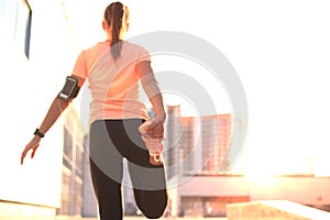 Young attractive sporty fitness woman runner warming up before run at sunset or sunrise on city.