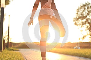 Young attractive sporty fitness woman runner warming up before run at sunset or sunrise on city.