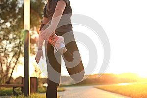 Young attractive sporty fitness woman runner warming up before run at sunset or sunrise on city.