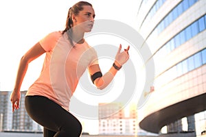 Young attractive sporty fitness woman running while exercising outdoors at sunset or sunrise in city.